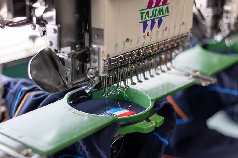 Machine de broderie Tajima qui réalise le marquage d'un logo brodé sur un vêtement